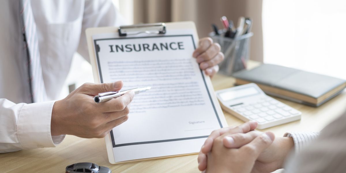 An commercial auto insurance agent explaining a policy document to a client across a desk with a calculator and notebook.
